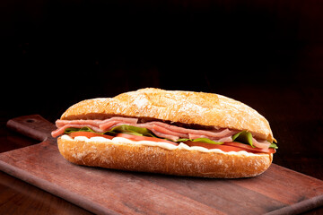 smoked carpaccio sandwich with arugula tomato and gruiere cheese on italian baguette on wooden board and dark background