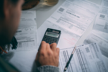 Close-up of a man's hands with a calculator and a lot of utility bills on the table. The man...