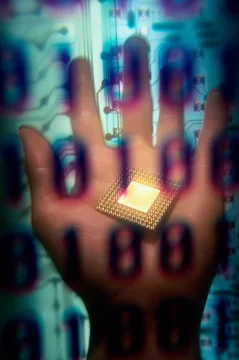Binary code superimposed over a person's hand holding a computer chip