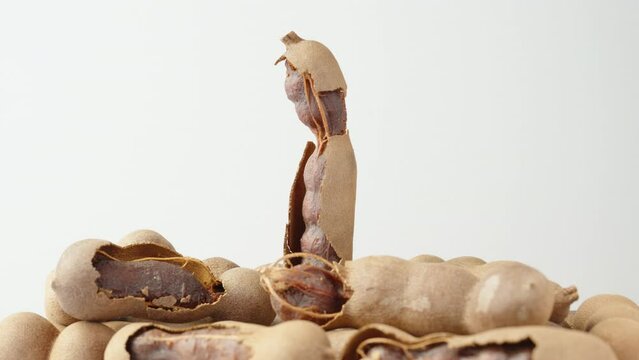 The tamarind fruit is half peeled, rotates on a white background on a handful of tamarinds.