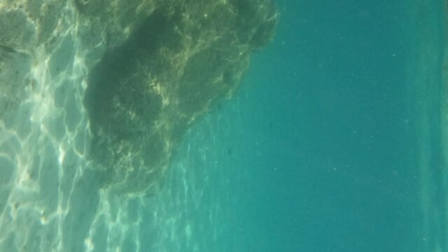 Underwater scene of ripple sunlight rays on sea bottom. Turquoise color seawater. Vertical screen.
