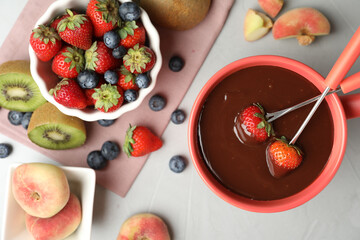 Dipping strawberries into fondue pot with chocolate on grey table, top view