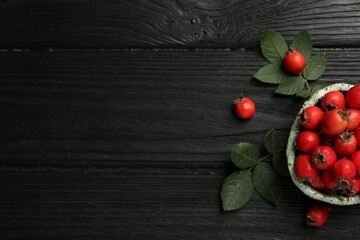 Ripe rose hip berries with green leaves on black wooden table, flat lay. Space for text