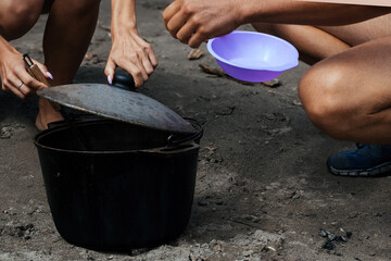 tourists, a man and a woman are pouring hot broth into plates, cooked outdoors on a fire in a large cast-iron pot