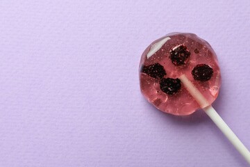 Sweet colorful lollipop with berries on lilac background, top view. Space for text