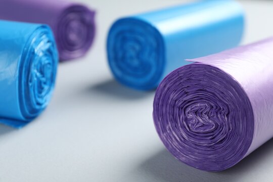 Rolls of different color garbage bags on light background, closeup