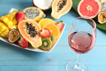 Delicious exotic fruits and glass of wine on light blue wooden table
