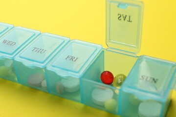 Plastic box with different pills on yellow background, closeup