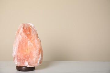 Himalayan salt lamp on table against beige wall. Space for text