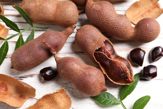 Delicious ripe tamarinds and leaves on white wooden table, closeup