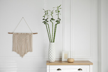 Vase with green bamboo stems on chest of drawers in room. Interior design