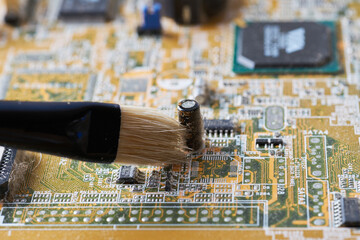 Brush cleaning an old motherboard from covering dust and dirt. Close-up.