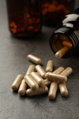 Overturned bottle with dietary supplement capsules on grey table, closeup