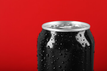 Black can of energy drink with water drops on red background, closeup