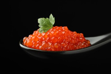 Spoon with delicious red caviar and parsley on black background, closeup