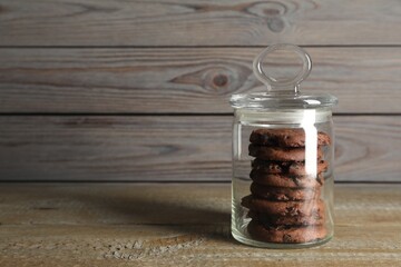 Delicious chocolate chip cookies in glass jar on wooden table, space for text