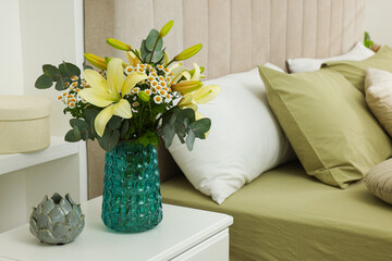 Bouquet of beautiful flowers and ceramic decor on nightstand in bedroom