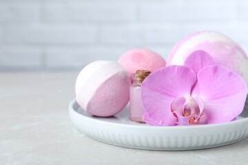 Colorful bath bombs, bottle of oil and orchid flower on grey table, closeup