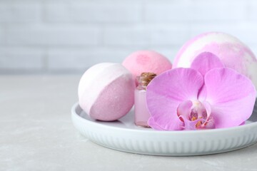 Colorful bath bombs, bottle of oil and orchid flower on grey table, closeup