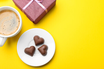 Cup of coffee, chocolate candies and gift box on yellow background, flat lay with space for text. Valentine's day breakfast