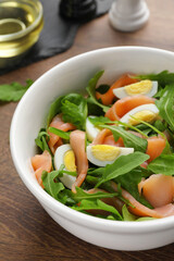 Delicious salad with boiled eggs, salmon and arugula on wooden table, closeup