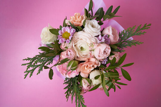 View from above. On a bouquet of roses, ranunculus, carnation, juniper, eustoma, bush chrysanthemum on a pink background. With a space to copy. An element for your design. High quality photo