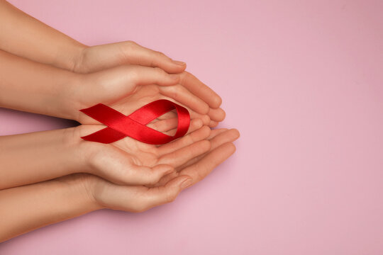 Woman and girl holding red ribbon on pink background, top view with space for text. AIDS disease awareness