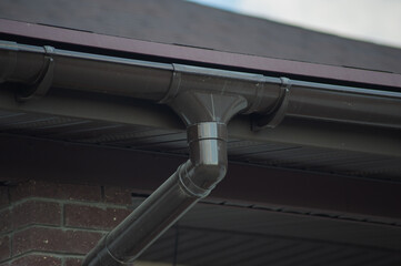 Corner of the house with new gray metal tile roof and rain gutter. Metallic Guttering System, Guttering and Drainage Pipe Exterior