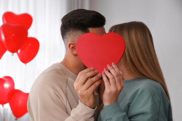 Fototapeta na wymiar Lovely couple kissing behind decorative heart at home. Valentine's day celebration