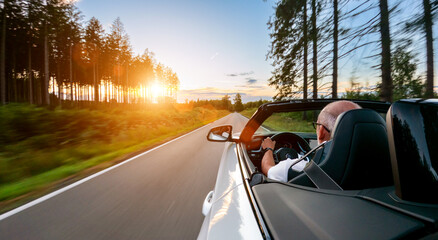 Fototapeta na wymiar Adult man is driving with convertable car in sunny nature on a bright summer day. wide angle pursuit shot with high speed motion blur