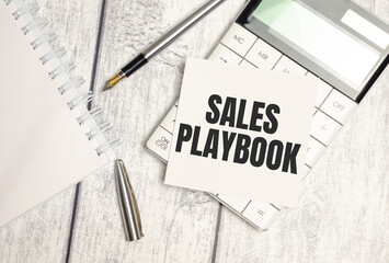 sales playbook, text on white sticker and calculator on wooden background