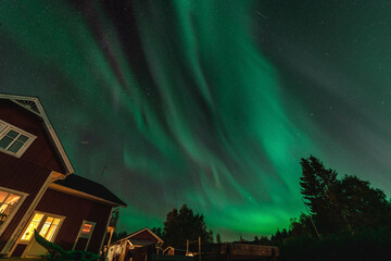 Dancing Northern lights Aurora borealis in autumn over backyard, part of house aside. Green Aurora high in sky. Umea town, Sweden, night. Copy space