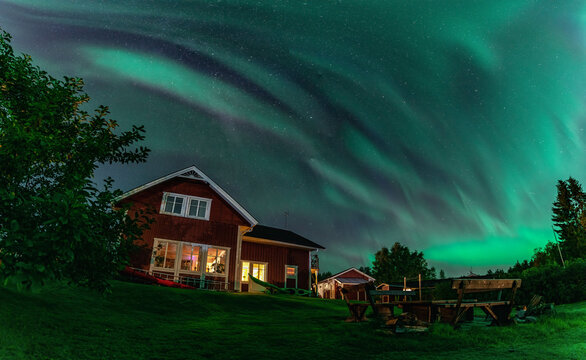 Panorama of dancing Northern lights Aurora borealis in autumn over wooden house, apple tree, tree benches in backyard. Umea town, Sweden, night. Copy space