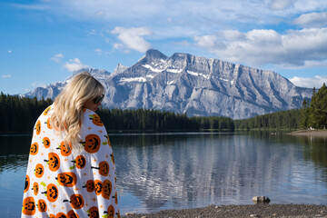 Relaxed young woman draped in a pumpkin blanket enjoys the view at Two Jack Lake in Banff National...