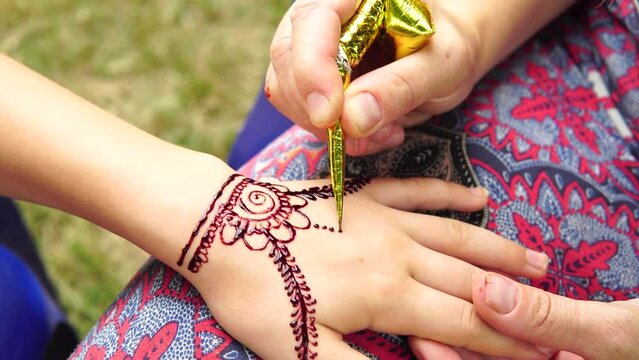 Drawing mehndi on the hand of a little girl closeup outdoors