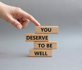 You deserve to be well symbol. Wooden blocks with words You deserve to be well. Beautiful grey background. Businessman hand. You deserve to be well concept. Copy space.
