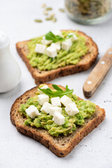 Toast with mashed avocado and feta cheese garnished with arugula leaf, closeup view