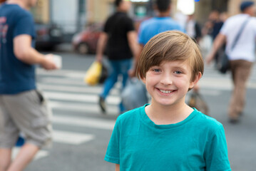portrait of a happy boy. the child is about to cross the road on a pedestrian crossing or zebra crossing. schoolboy in front of the road and crowds of people crossing the roadway