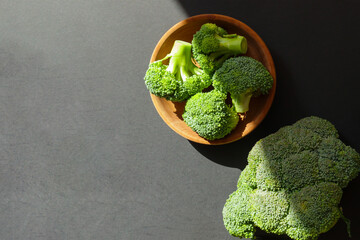 Broccoli in wooden bowl, on dark background, top view.