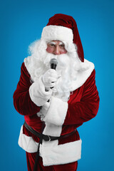 Fototapeta na wymiar Santa Claus singing with microphone on blue background. Christmas music