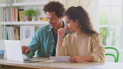 Couple at home using laptop to check bills and home finance preparing a business plan for online store - shot in slow motion
