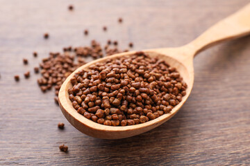 Spoon with buckwheat tea granules on wooden table, closeup