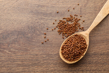 Spoon with buckwheat tea granules on wooden table, top view. Space for text
