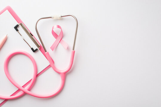 Top view photo of pink ribbon symbol of breast cancer awareness stethoscope pen and clipboard on isolated white background with copyspace