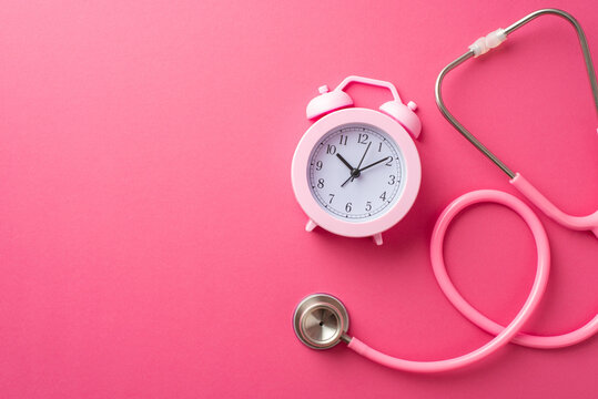 Breast cancer awareness concept. Top view photo of pink stethoscope and alarm clock on isolated pink background with copyspace