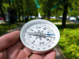 A compass in person's hand in park. Orient yourself in current situation (urban conditions). Follow...