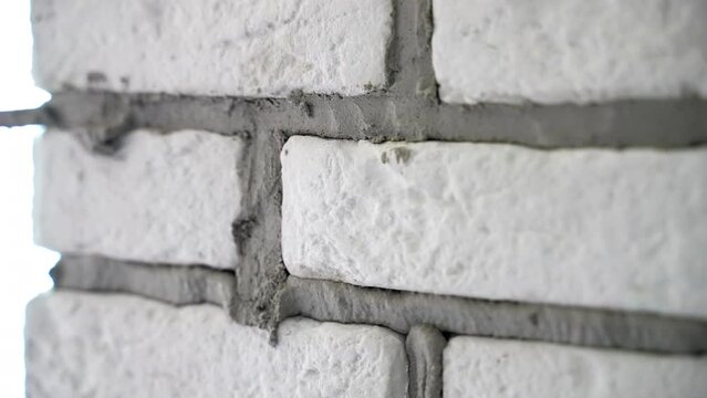 Close up shot of renovates wall with decorative stones, workman grouting joints with special grout spatula, renewal works with wall on construction site