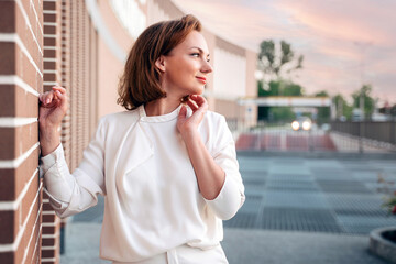 Fototapeta premium Beautiful smiling caucasian woman wearing stylish clothing looking away on the street, copy space