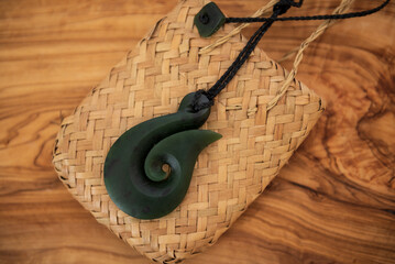 Pounamu fish hook necklace on grainy wooden background. Aotearoa, New Zealand, Maori. Side angle view.