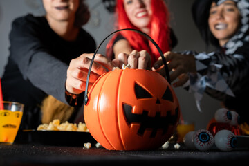 Group of friends in a halloween party taking popcorns from a pumpkin shaped container